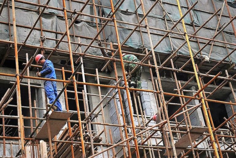 two people on the scaffolding of a construction site with personal protective equipment